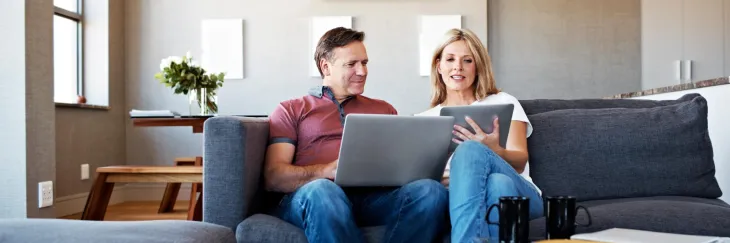 Couple in living room looking at laptop and tablet.