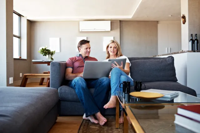 Couple in living room looking at laptop and tablet.