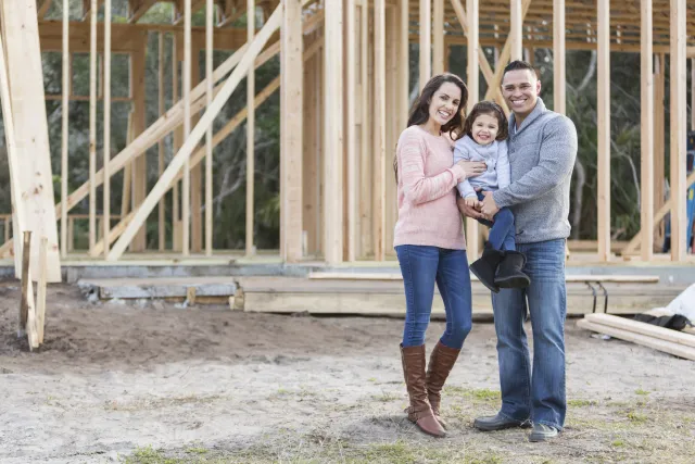 couple and child standing outside of their home construction site